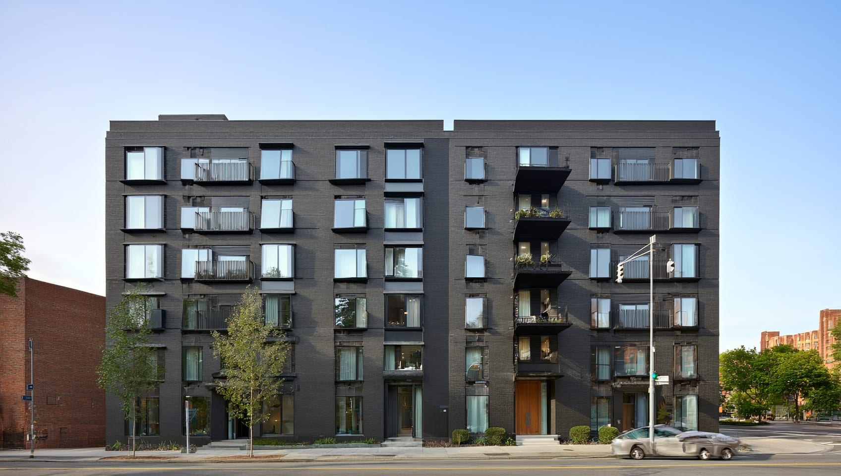 Daytime street-level photograph of a modern apartment building with charcoal brick high-street architecture