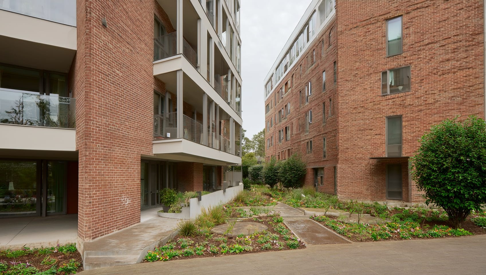 Angled daytime exterior of a modern brick mixed-use apartment building with landscaped entrance planters