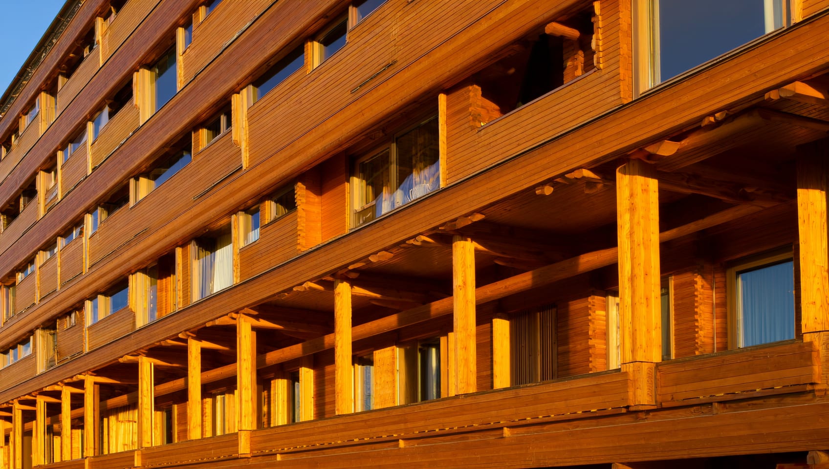 Close angle of a mass-timber residential building facade showing exposed wood beams and large windows