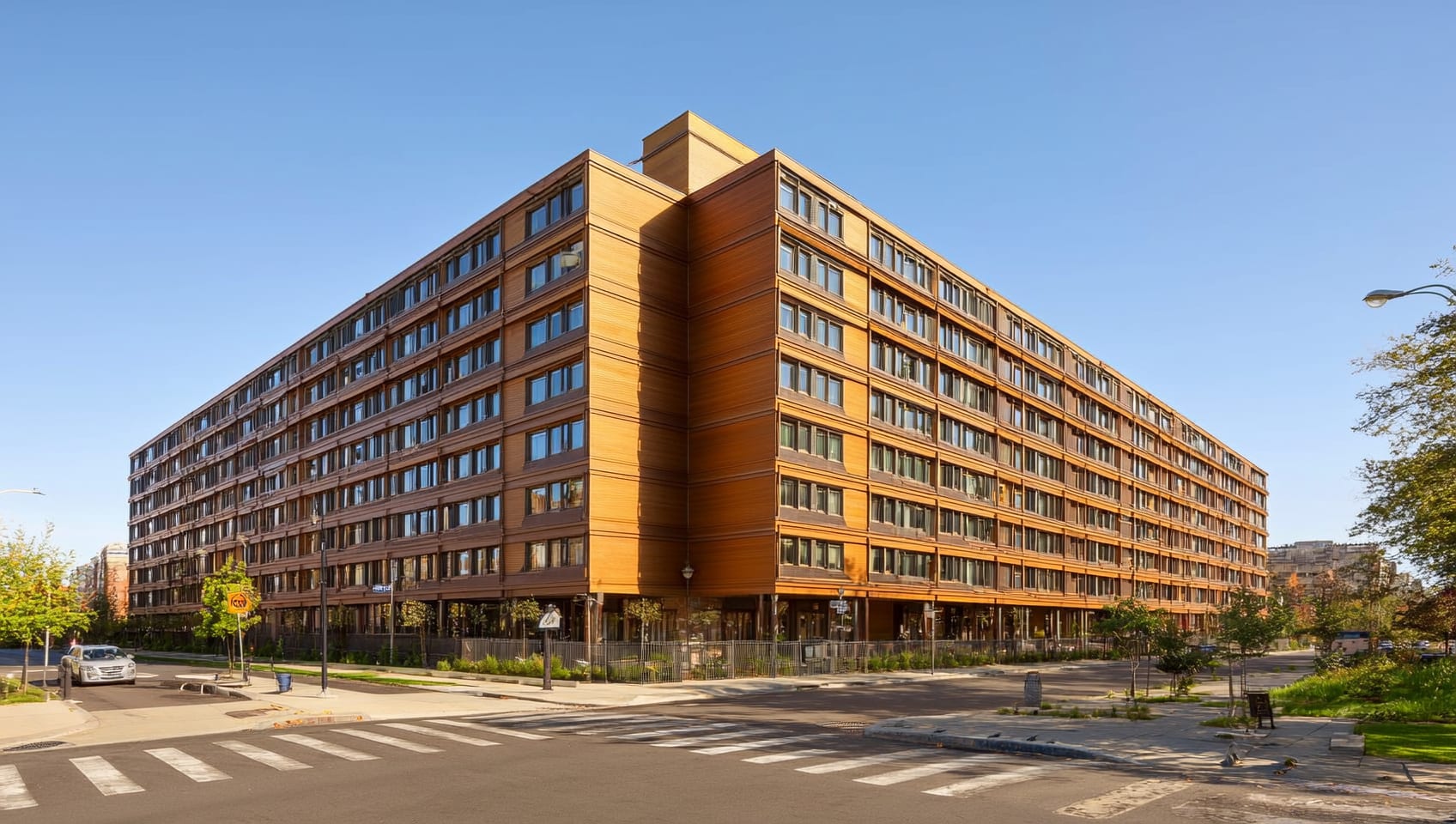 Completed mass-timber apartment building with warm wood accents on a sunny riverside street